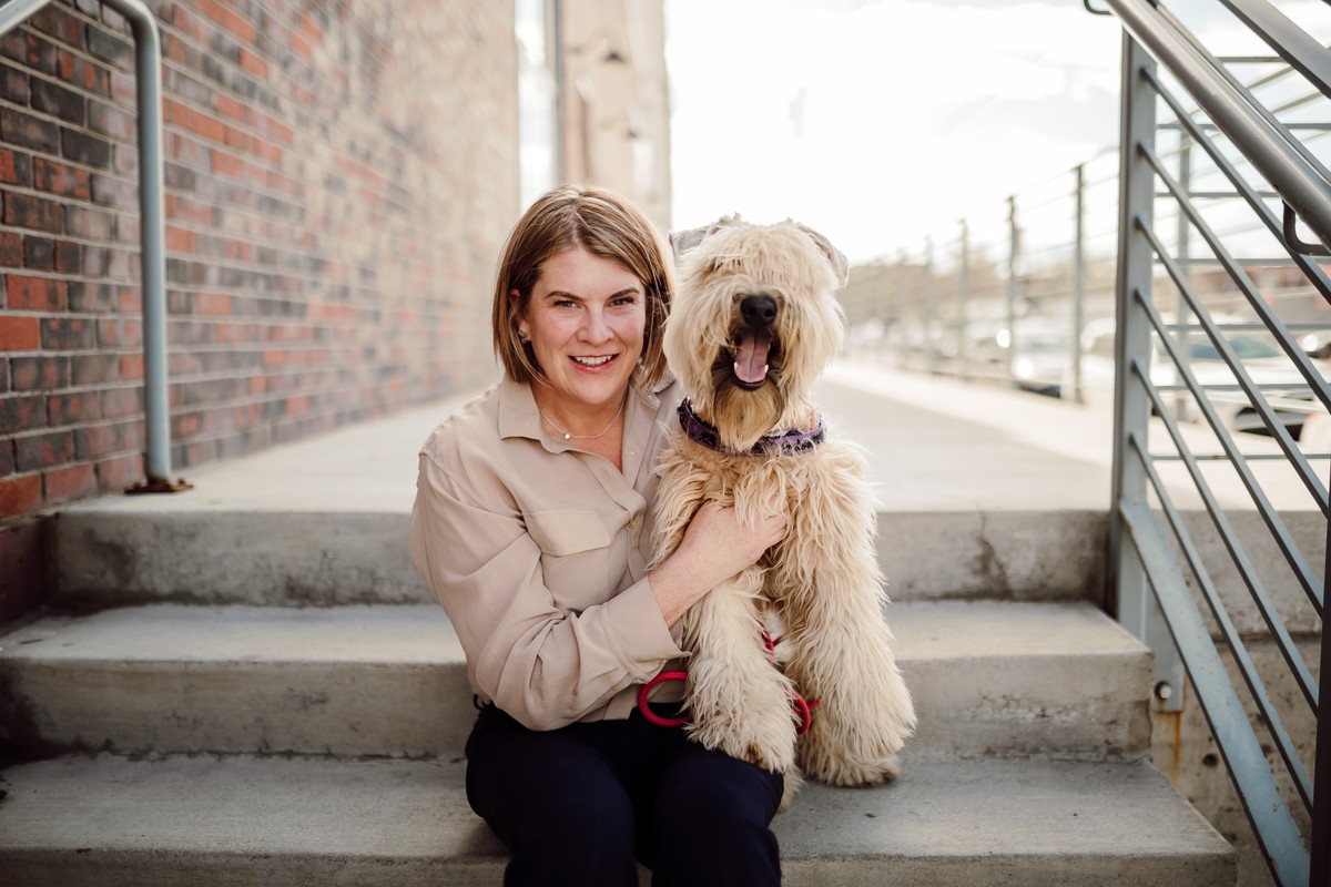 Client seated on concrete steps, smiling with a shaggy wheaten dog in her arms