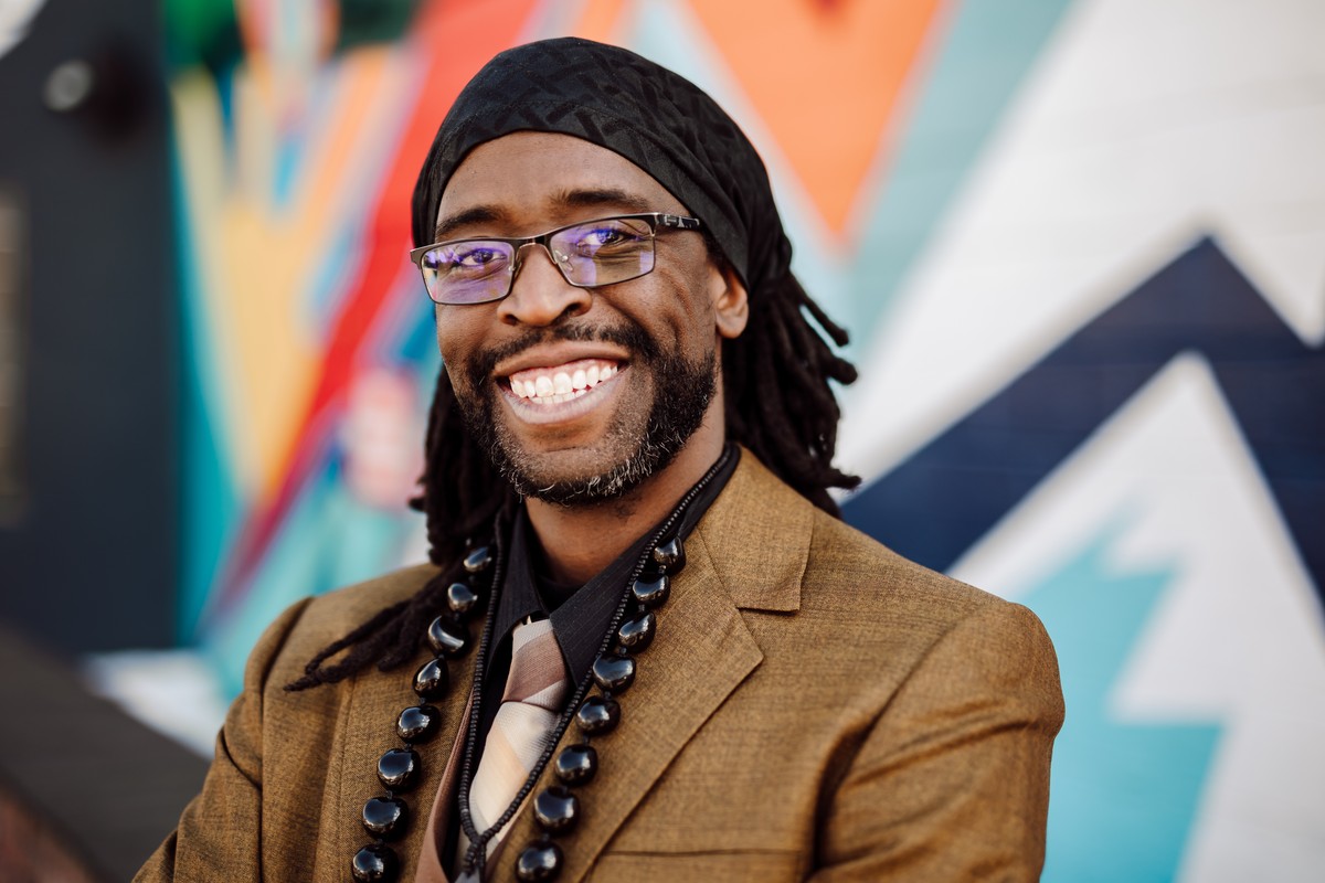 Headshot client in glasses and a tan blazer with beaded necklaces, smiling in front of a colorful mural