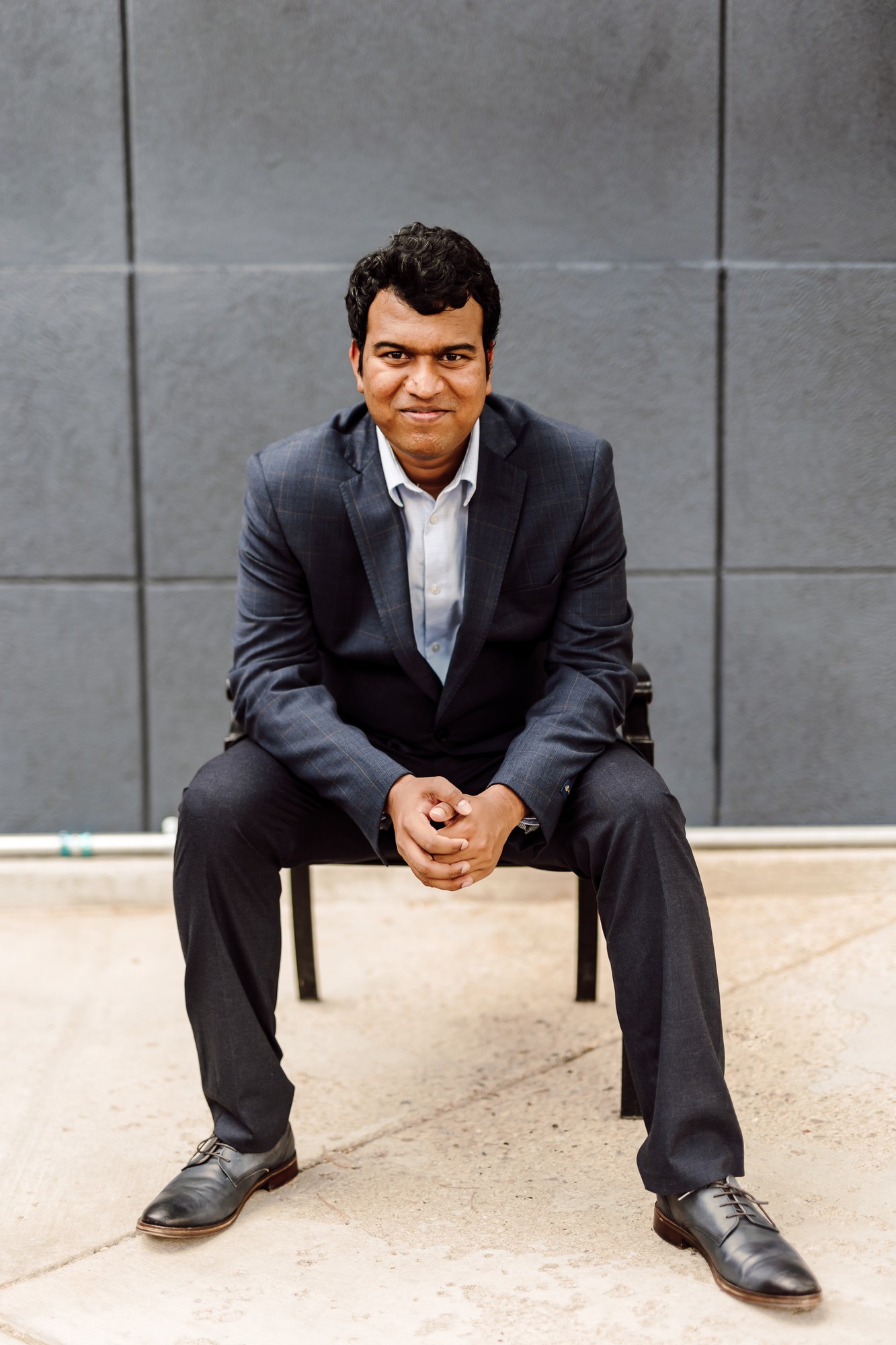 Headshot client in a dark suit seated on a bench in front of a slate wall