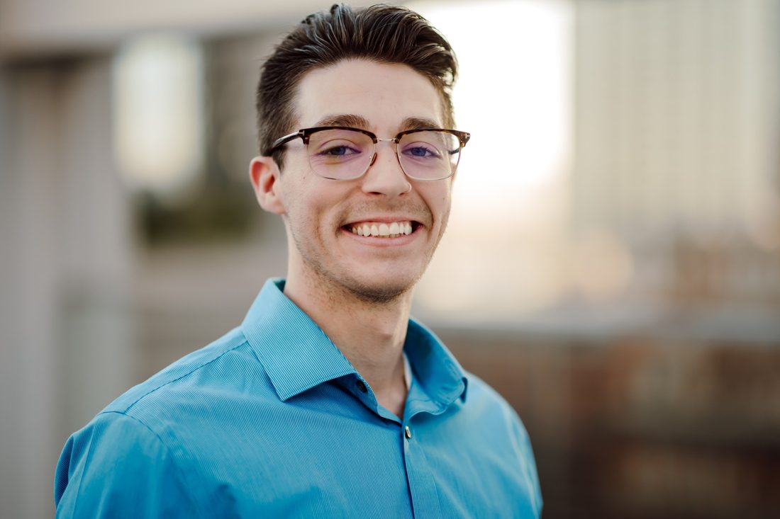 Headshot client in glasses and a blue shirt, smiling in warm evening light